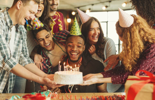 Happy birthday boy looking on cake with candles surronding friends